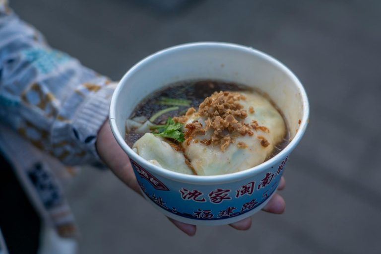Close-up of flavorful dumpling soup in a disposable bowl held outdoors.